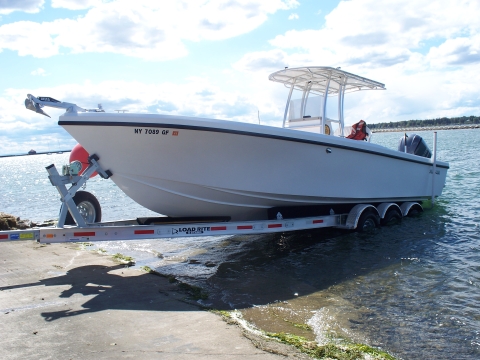 A fiberglass-hulled boat with a bimini top over the console being launched from a trailer at a boat ramp