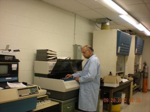 A balding person with medium skin tone wearing a lab coat puts samples into a lab instrument