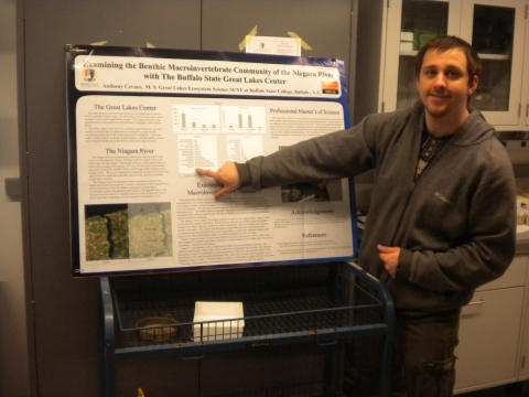 A person stands next to a poster, pointing out a figure on the poster.