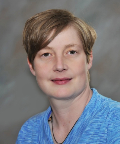 A person with a short pixie cut and a light blue shirt with a cord necklace