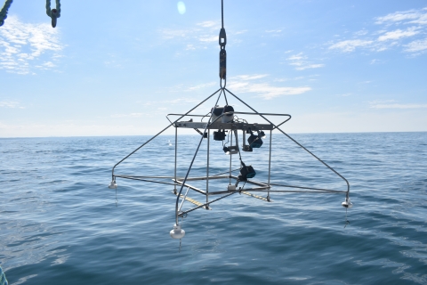 A frame with video equipment being held above the surface of the water by a cable