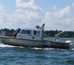 An aluminum-hulled boat throwing wake in Lake Erie. A person peeks out of the front of the boat.