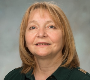 portrait of Lyubov Burlakova, a light-skinned person with shoulder-length blonde hair, dark grey eyes, wearing a green collared shirt