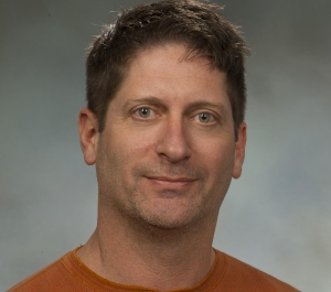 portrait of Christopher Pennuto, a light-skinned person with grey eyes and cropped brown hair wearing an orange shirt with three buttons at the collar