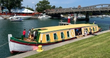 A historic painted wooden boat in a canal. The boat has a long low cabin taking up most of the length