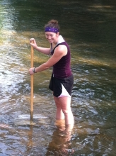 A student wading in a shallow stream with a rectangular net on a pole under the water