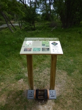 A printed informational sign on two posts. At the base is a boot brush, designed to brush the sides and bottom of a boot.