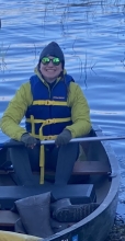 A person in cold weather gear and a life jacket sits in a canoe in a wetland