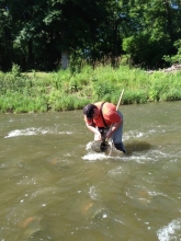 A person in chest waders stands in a stream emptying a trap into a net on a pole