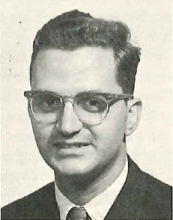 black and white portrait of a person with thick framed glasses in a suit and tie