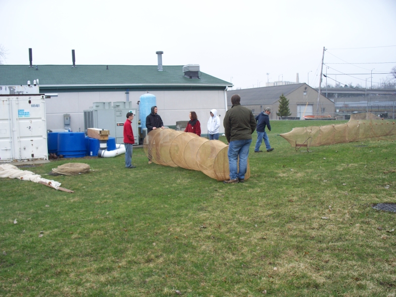 A group of people sets up two long cylindrical nets in a field. A few more nets lie on the ground.