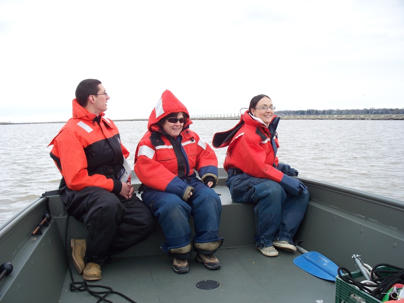 Three people sitting at the front of a boat wearing coldwater safety gear