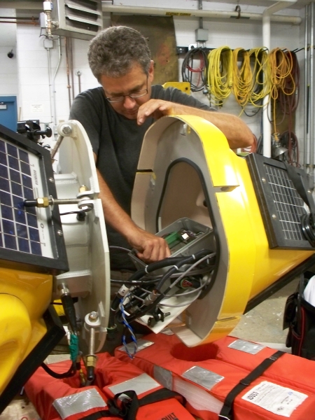 A person working on the electronics in the middle of a yellow fiberglass buoy