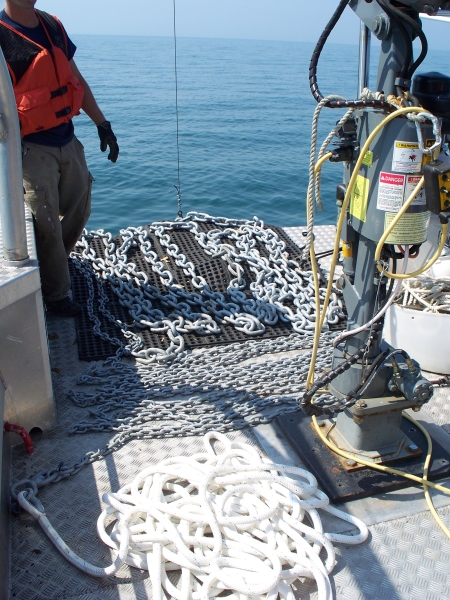 a person stands near chain and rope laid out on the deck of a landing craft boat with the bow door down