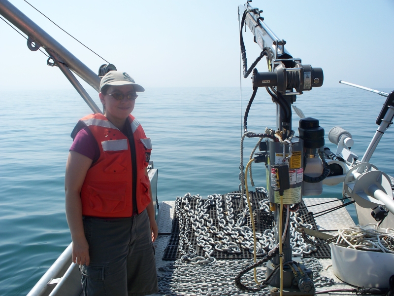 a person smiles and stands near chain laid out on the deck of a landing craft boat with the bow door down