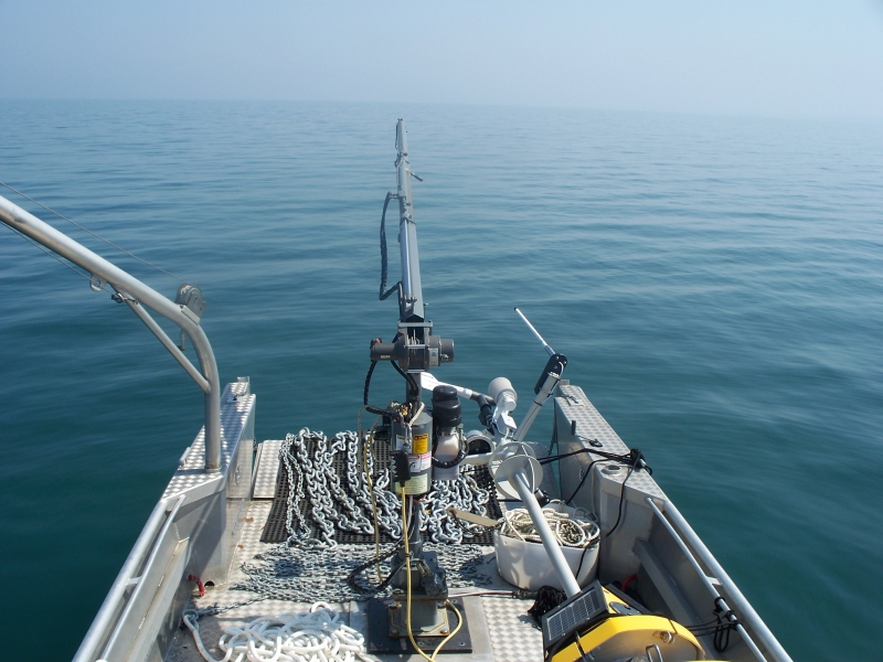 The deck of a landing craft boat with the bow door open and anchor chain and rope laid out, and a buoy lying on the deck, on a calm, clear day with no distinction between the water and sky