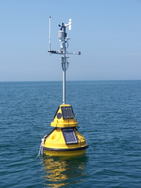 A yellow buoy with meteorological instruments and solar panels sitting in the water, rotated slightly