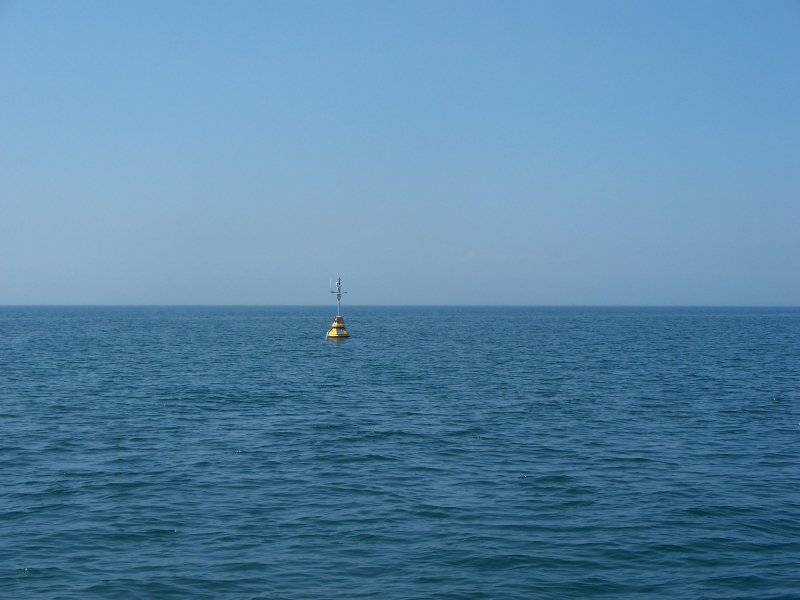 A fiberglass buoy with a mast in the distance on a lake