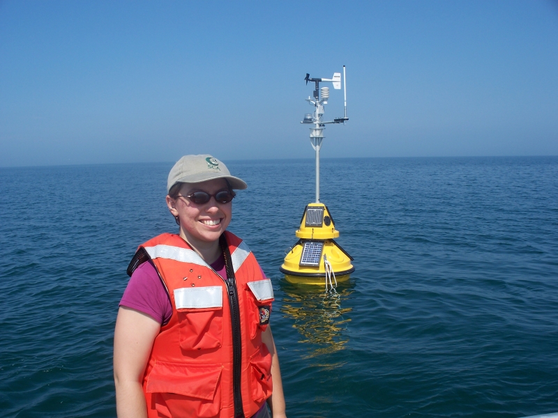 A person in a life jacket stands near a buoy that is floating in the water