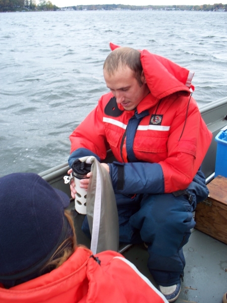 A person in coldwater safety gear on a boat holds the cup at the bottom of a plankton net