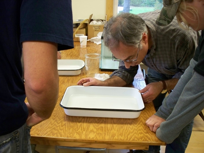 A person with glasses looks into a porcelain pan filled with water on a table