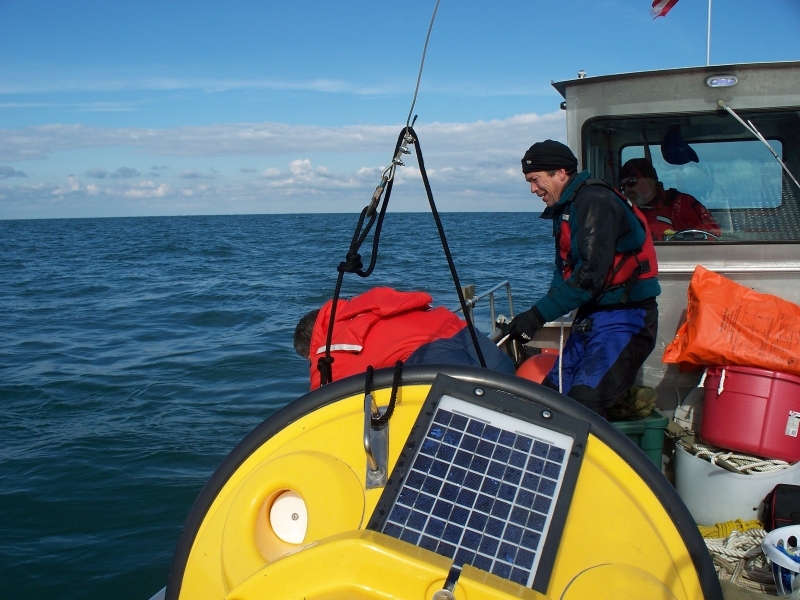 A buoy lies on the deck of a boat with two people working nearby