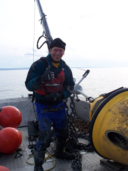 A person standing on the deck of a boat gives a thumbs up, standing next to a buoy lying on the deck.