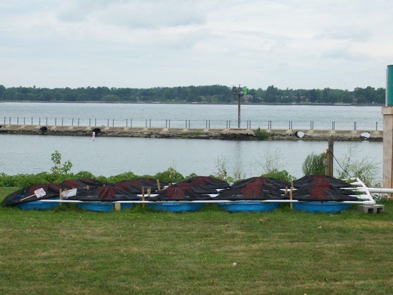 An array of pools covered by mesh and connected with pipes at the waterfront.