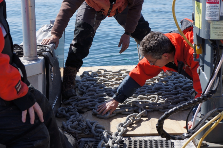 Two people work to neatly lay out a chain in the bow of a landing craft boat with the bow door down