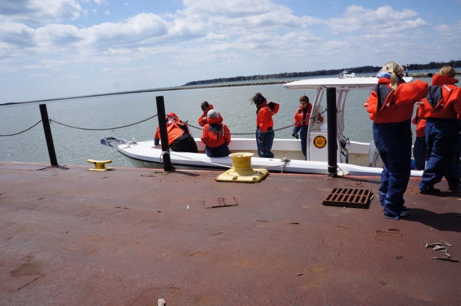 People in coldwater safety gear step on board a fiberglass boat tied up at dock