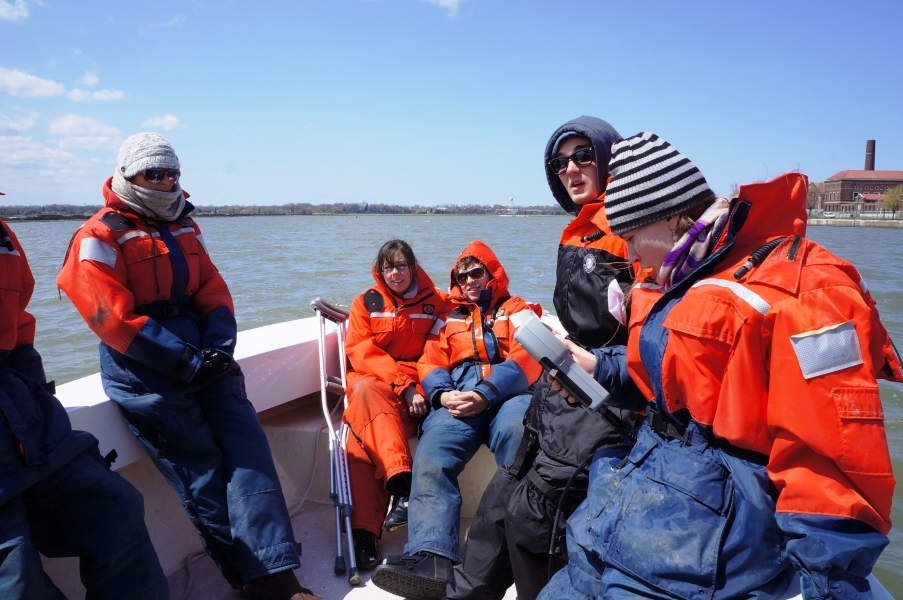 Students sitting in the front of the boat. One holds a sampling instrument. One of the students has crutches.