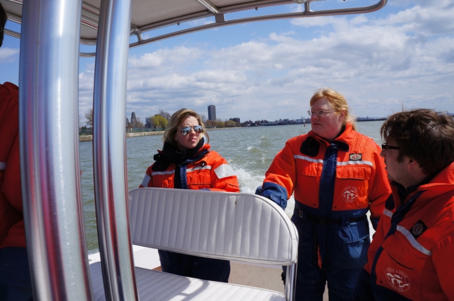 Three people standing at the back of the boat behind a seat