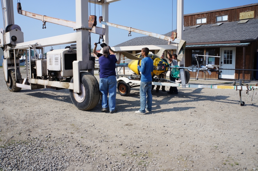 A few people work to position straps on a metal frame. The straps are connected to a buoy on a trailer