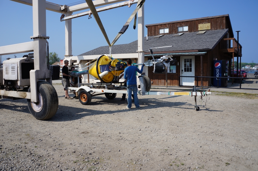 A strap on a large metal frame begins to lift a buoy from a trailer.