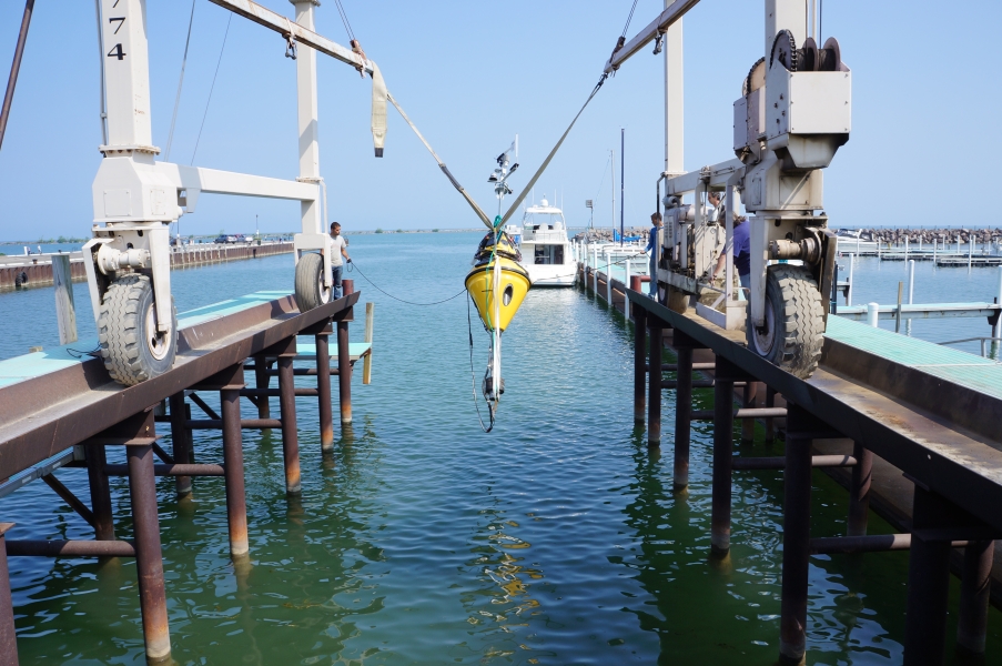 A buoy hangs over the water from a strap on a large metal frame.