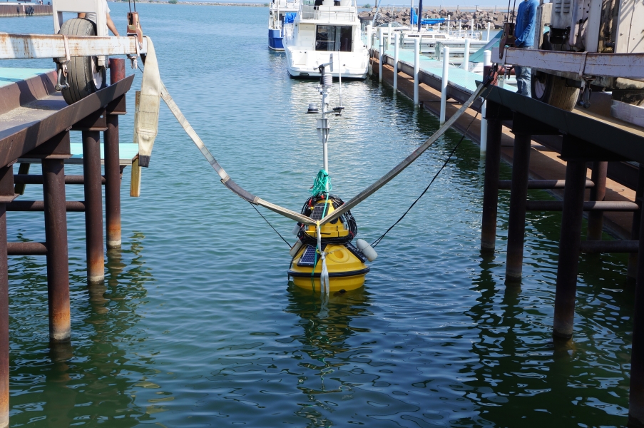 A buoy sits in the water at the end of a boat slip. Straps still connect it to a large metal frame.