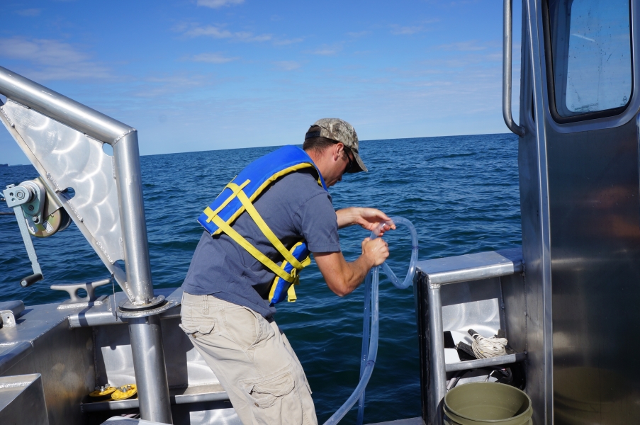 A person begins to pull up a tube over the side of a boat, squeezing part of the tube tightly to pinch it