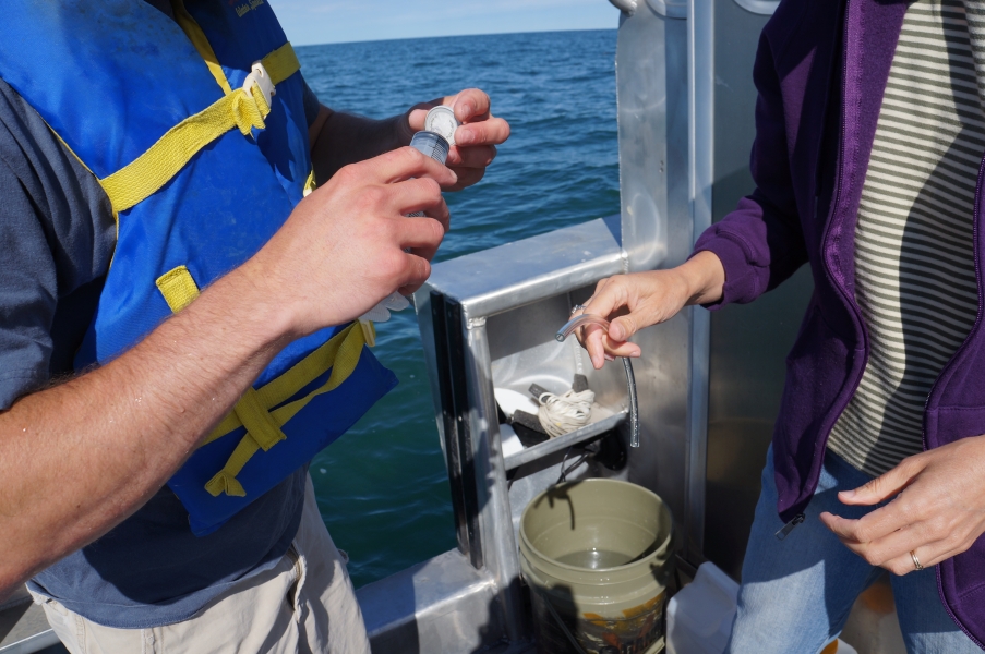 A person on a boat attaches a filter to a syringe while a second person holds a small thin tube