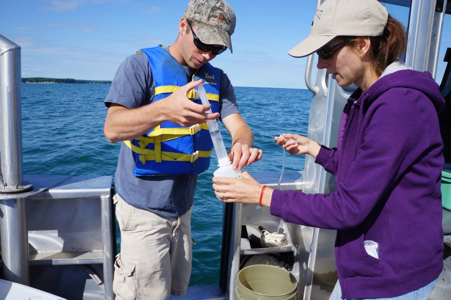 A person on a boat empties a syringe into a bottle that a second person is holding