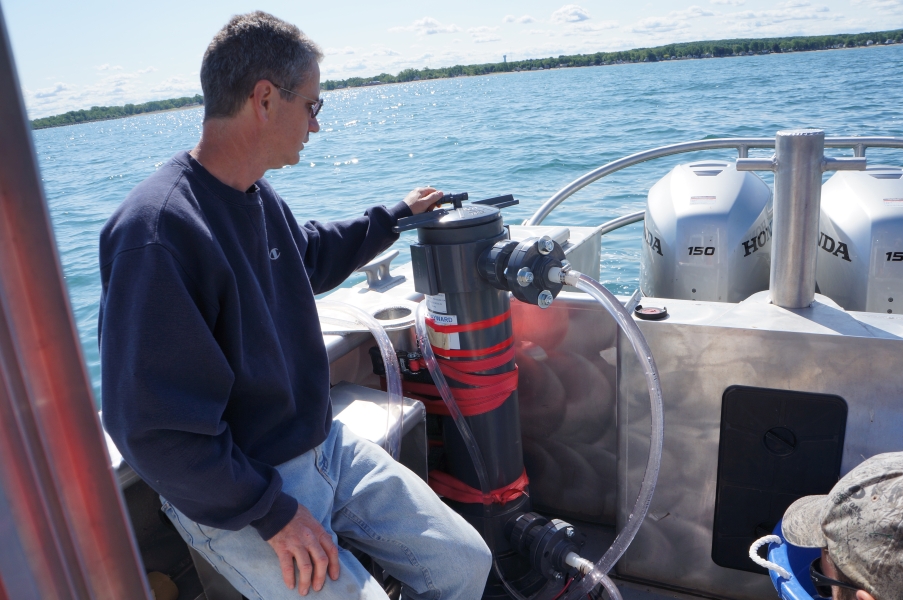 A person sits on a boat next to a PVC cylinder with tubes running out of it