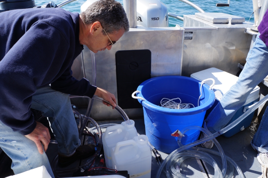 A tube is coiled on the deck of a boat. A person holds one end into a jug