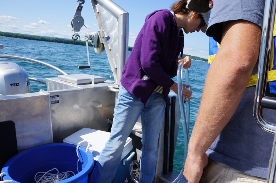 A person lowers a tube into the water over the side of a boat while a second person stands nearby