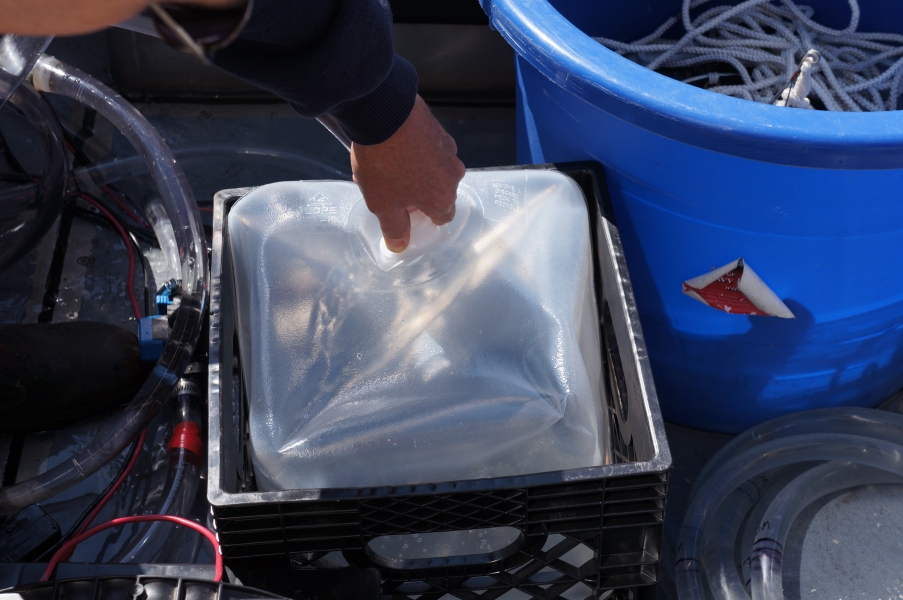 A person holds a tube into a cube container to fill it with water