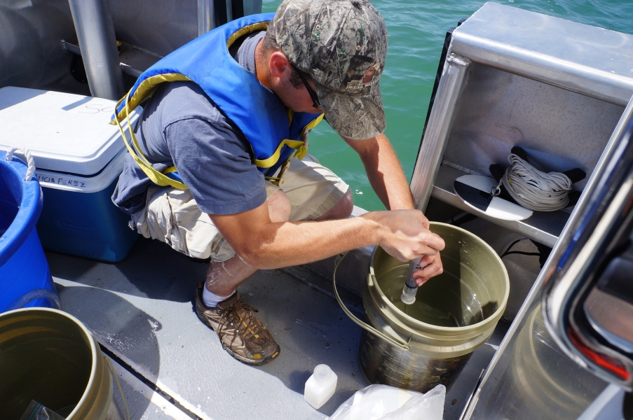 A person on a boat kneels over a bucket with a syringe filter