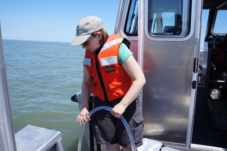 A person in a life jacket lowers a tube over the side of a boat