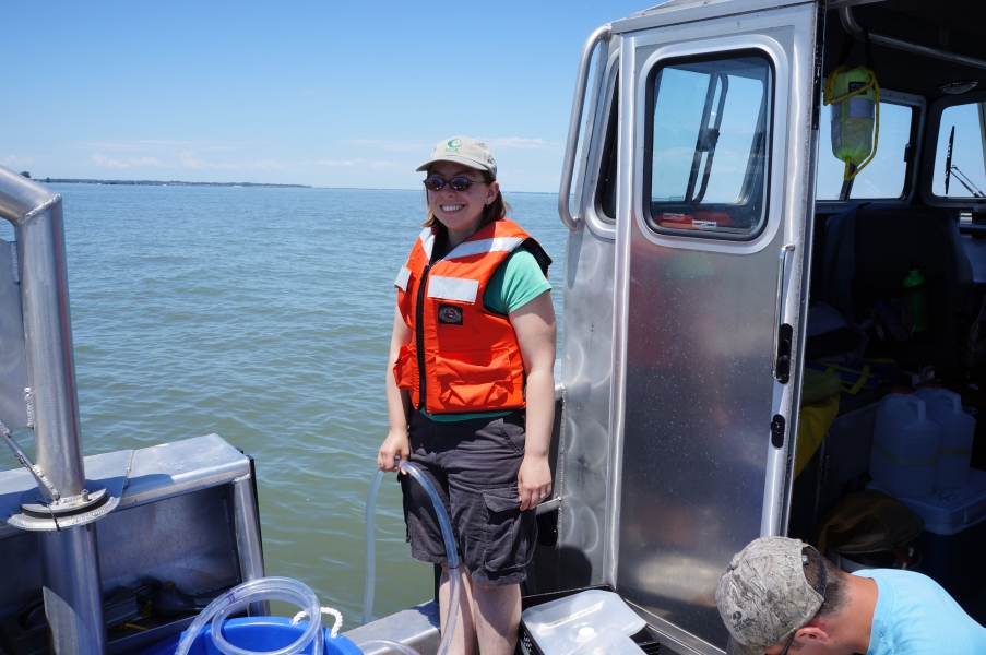 A different person stands in the back of a boat, holding a tube in the water