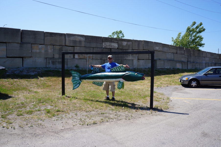 A person stands by a sign in the shape of a large green fish