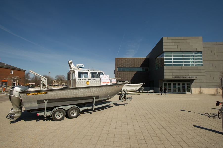 a boat sits on a trailer in front of a building with a placard for the 50th anniversary of the Great Lakes Center. There is a second boat behind the first boat.