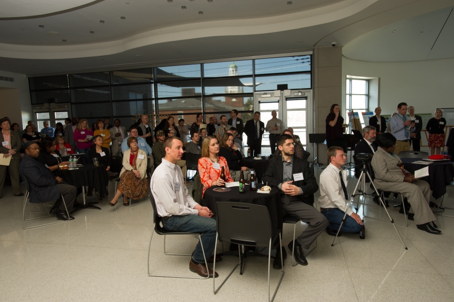 Guests seated around tables and standing while they watch something off to the right