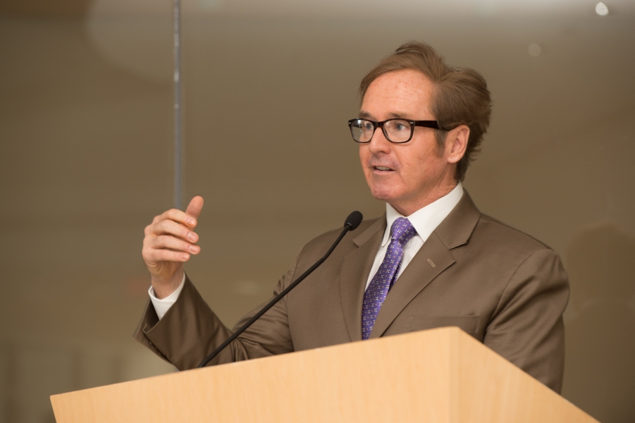 a person in a suit with glasses stands behind a podium